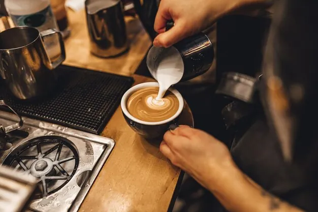 A barista pouring steamed milk to make a latte, a key step in creating several popular types of coffee drinks.